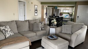 A living room with a grey sofa set, a coffee table with books, and a kitchen in the background. - Lake Ozark Condo- Come stay & play! (Lake Ozark)