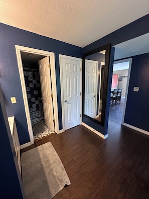 A hallway with a dark blue wall, a white door, and a mirror reflecting a dining area.