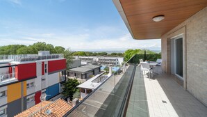 Un balcón con barandilla de vidrio que da a un paisaje urbano, con edificios modernos y cielo despejado.
