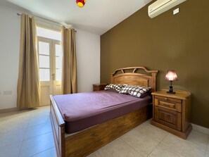 Een slaapkamer met een houten bed, een nachtkastje met een lamp en een raam met gordijnen.