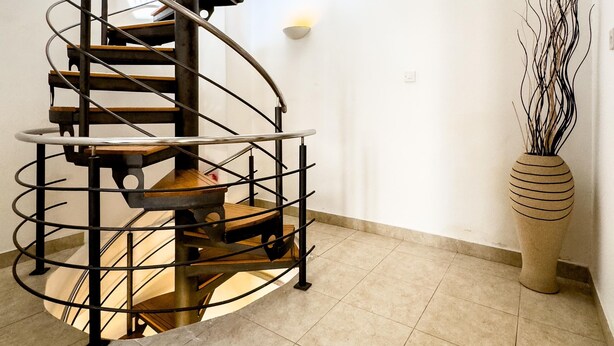 A modern spiral staircase with metal railings and wooden steps, leading to an upper floor.