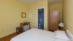 Een slaapkamer met een bed, een bureau, een stoel, een kledingkast, en een zichtbare badkamer door een geopende deur.