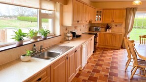 Een keuken met houten kastjes, een spoelbak, een magnetron en een eethoek met stoelen.