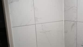 A shower with white marble tiles and a visible metal fixture.