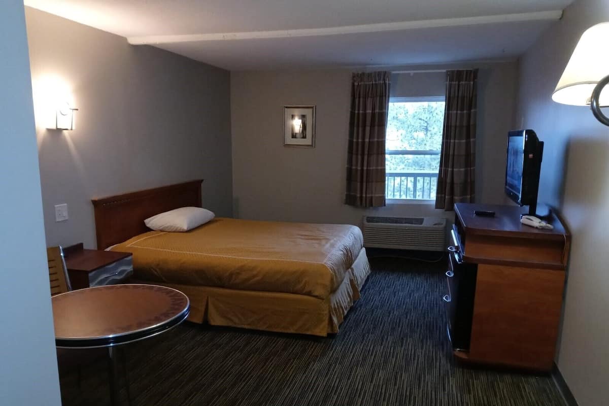 A hotel room with a bed, a desk, a chair, a television, and a window with curtains.