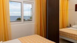 A hotel room with a bed, a window with curtains, a view of the sea, and a wooden floor. - Apartments Villa Marijana - Two Bedroom Apartment with Terrace and Sea View (Prižba)