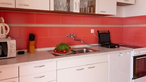 A modern kitchen with white cabinets, a red backsplash, a sink, a toaster, a kettle, and a stove. - Apartments Villa Marijana - Two Bedroom Apartment with Terrace and Sea View (Prižba)
