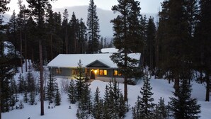 Una cabaña cubierta de nieve rodeada de altos pinos.