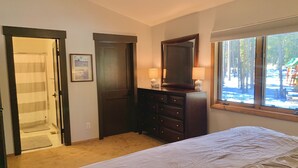 Un dormitorio con cama, cómoda, espejo y ventana con vista a árboles.