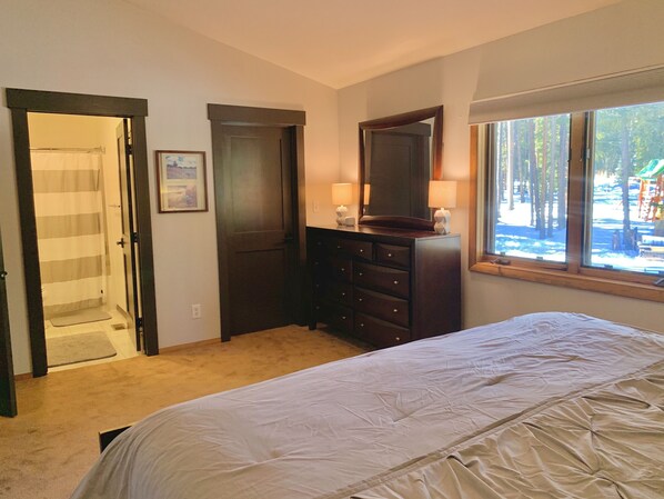 A bedroom with a bed, a dresser, a mirror, and a window with a view of trees.