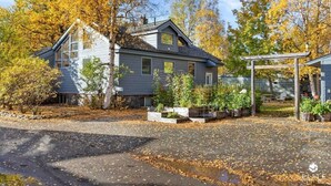 A two-story house with a garage, surrounded by trees with autumn foliage. - The Fireweed Gardens (Anchorage)