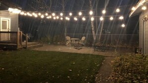 A backyard with a covered patio area, string lights, and outdoor furniture. - The Fireweed Gardens (Anchorage)
