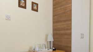 Een kleine kamer met een houten bureau, een witte koelkast, een klein kastje en een kledingkast.