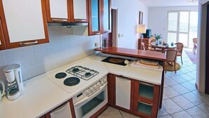 Une cuisine compacte avec des meubles blancs, une cuisinière à gaz, une machine à café et un coin repas comprenant une table et des chaises.