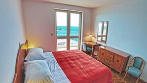 Une chambre à coucher comprenant un lit, un bureau, une chaise et une vue sur la mer, accessible par une porte coulissante.