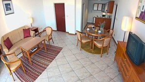 Un espace de vie compact comprenant un canapé, une table à manger, des chaises, un téléviseur et un coin cuisine.