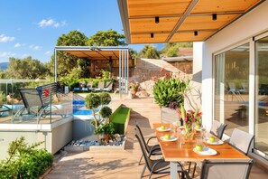 A modern outdoor dining area with a pool, seating, and a view of the landscape.