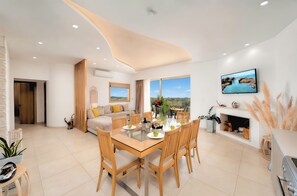 A modern living room with a dining area, a fireplace, and a large TV on the wall. - Canes Villa Heated Pool (Agios Nikolaos)