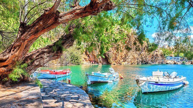 Un sentier de pierres mène à des bateaux amarrés dans une étendue d’eau d’un bleu limpide, le tout étant entouré de falaises rocheuses et de verdure.