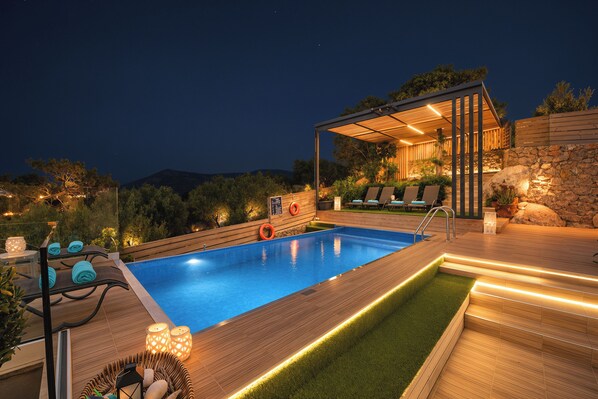 A swimming pool with a wooden deck, lounge chairs, and a covered seating area.