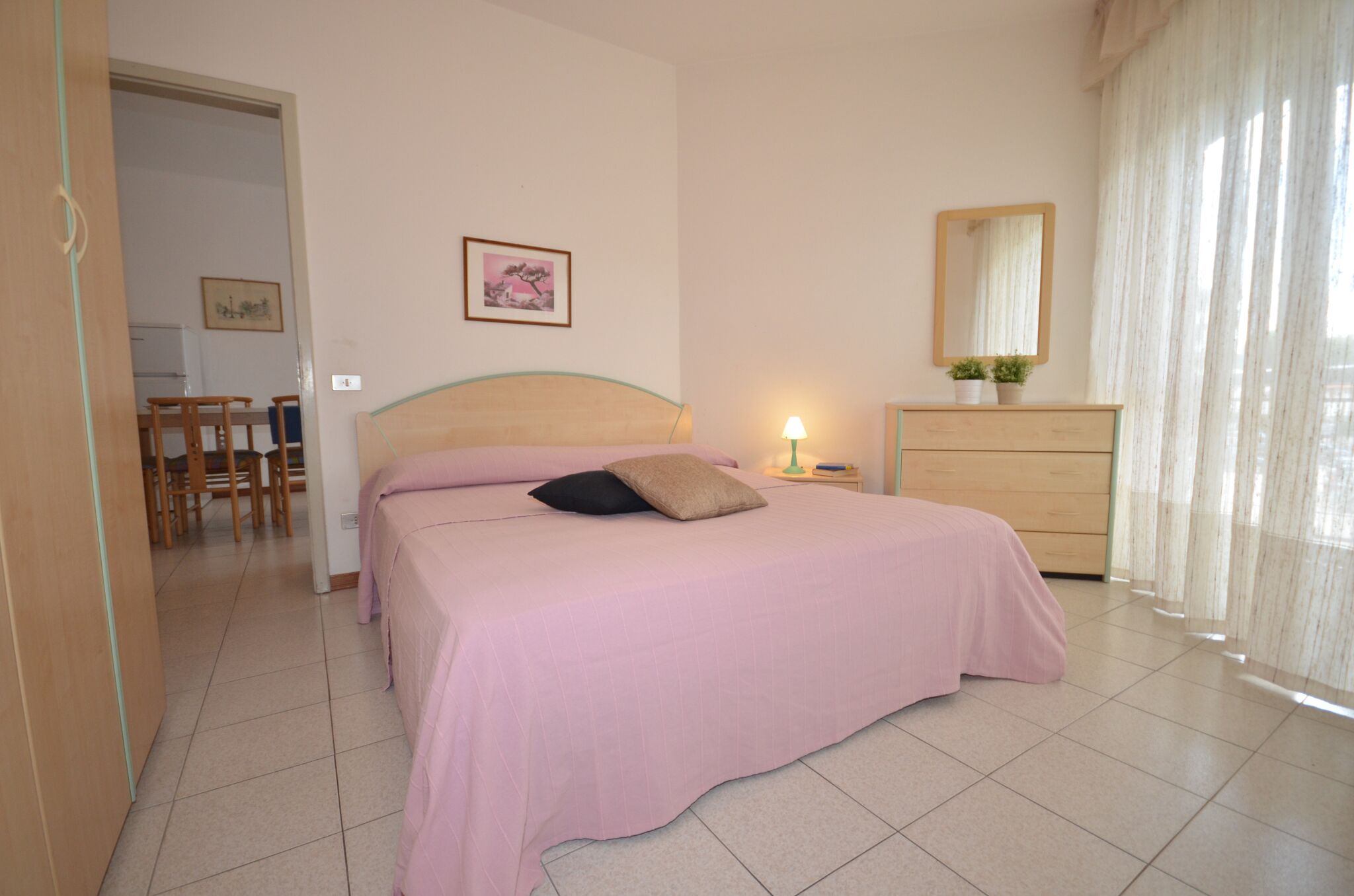 Une chambre à coucher avec un lit, une commode, un miroir et une petite table avec une lampe.
