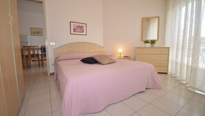 A bedroom with a bed, a dresser, a mirror, and a small table with a lamp.