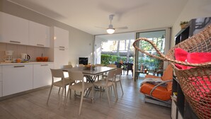 Une cuisine moderne avec des meubles blancs, un coin repas comprenant une table et des chaises, et un fauteuil en osier avec un coussin rouge.