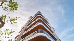 Ein modernes Mehrfamilienhaus mit geschwungenen Balkonen und einer Kombination aus Glas- und Holzelementen.