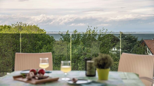 Ein Tisch mit Speisen und Getränken, mit Blick auf eine malerische Landschaft aus Bäumen und einem Gewässer.
