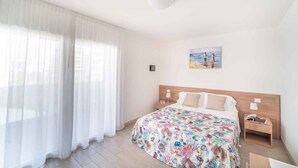 Ein Hotelzimmer mit Bett, Nachttisch, Lampe, einem Bild an der Wand und durchsichtigen Vorhängen.