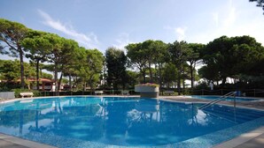 A clear blue swimming pool surrounded by trees and a clear sky.