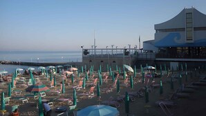 A beach with rows of sun loungers and umbrellas, a building with a wave design, and a clear view of the sea.
