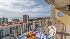 A balcony with a table holding fruit, a chair, and a view of the beach and buildings.
