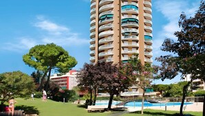 A tall, cylindrical hotel with multiple balconies, surrounded by lush greenery and a swimming pool.