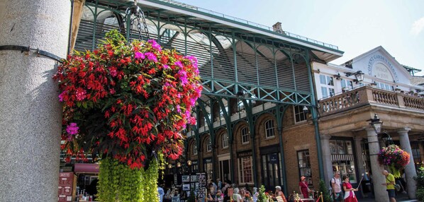 A bustling market with a prominent hanging flower display and traditional architecture.