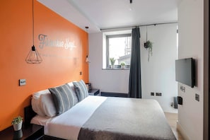 A modern hotel room with a large bed, a TV, a window with a view, and a wall with a motivational quote.