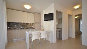 A modern kitchen with white cabinets, a marble countertop, and a dining area with white chairs.