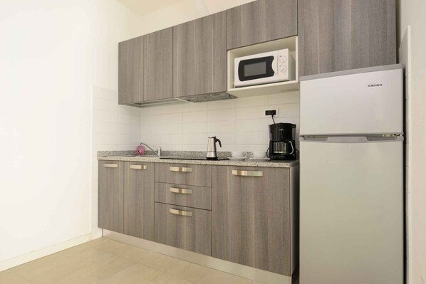 A modern kitchen with grey cabinets, a microwave, a coffee maker, and a refrigerator.