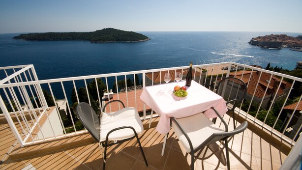 A balcony with a table set for two, overlooking a coastal view with a small island and a fortified structure.