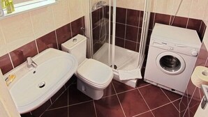 A bathroom with a sink, toilet, shower, and washing machine.