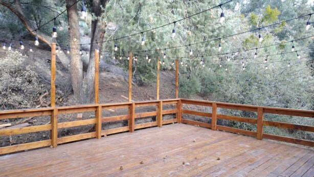 A wooden deck with a railing, surrounded by trees and string lights. - Mt. Pinos adjacent Mountain Cabin (Frazier Park)