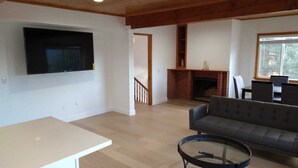 A spacious living room with a flat-screen TV mounted on the wall, a fireplace, a sofa, and a dining area with chairs. - Mt. Pinos adjacent Mountain Cabin (Frazier Park)