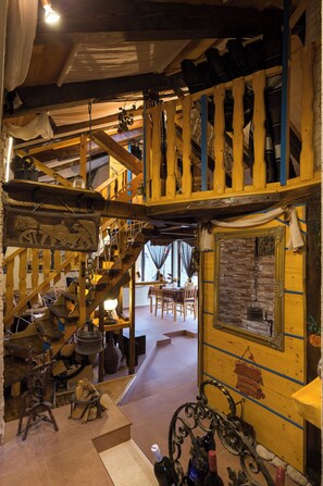 Staircase leads to an upper level, flanked by wooden structures and a table with a lamp.