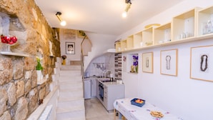 A compact kitchen with a stone wall, a dining area with a table, and a staircase leading to a second floor.