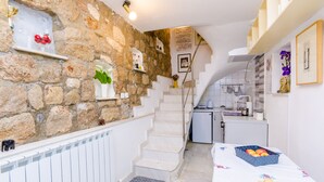 A kitchen with a stone wall, white cabinets, and a staircase leading to another level.