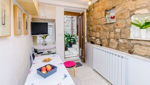 A compact kitchen with a stone wall, a dining table with fruits, and a TV.