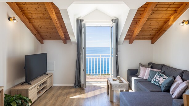 Un salon confortable avec une télévision, un canapé et un balcon offrant une vue sur la mer.