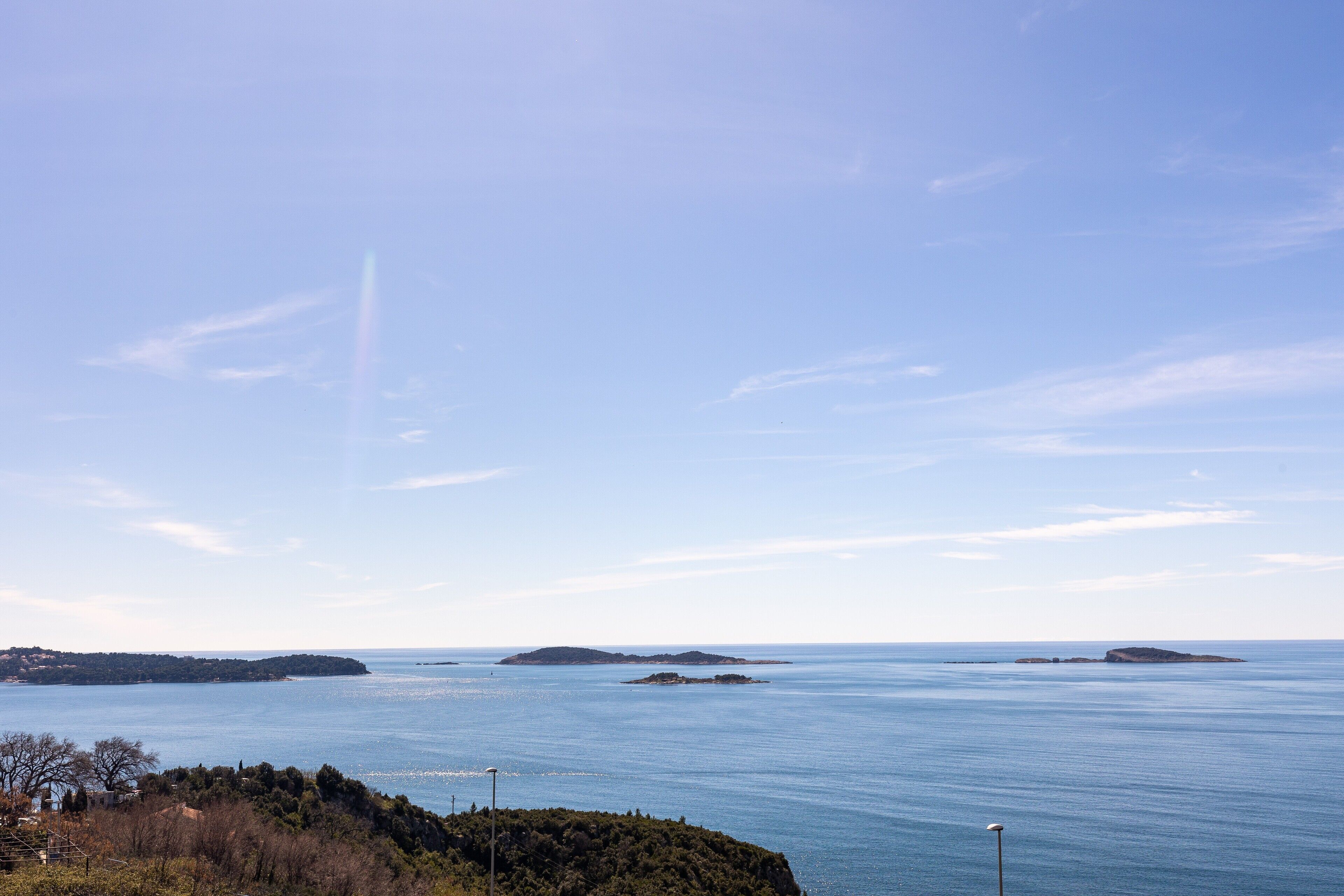 A coastal landscape with a clear sky, calm sea, and distant islands.