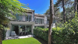Una casa moderna de dos pisos con balcón, un patio con mobiliario exterior y un jardín bien cuidado.