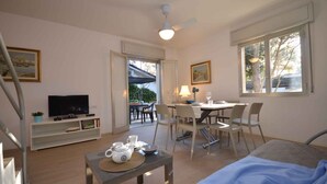 Una habitación con cama, televisor, mesa de comedor con sillas, una mesita con tetera y ventana con vista a árboles.
